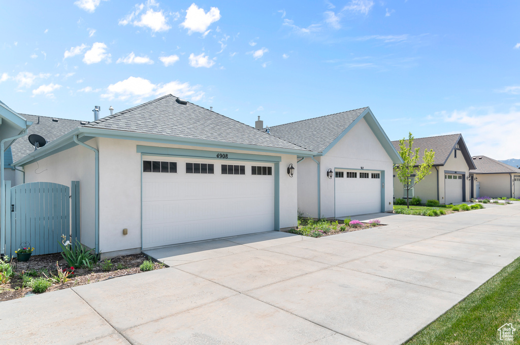 View of front of property featuring a gate, stucco siding, roof with shingles, driveway, and a garage