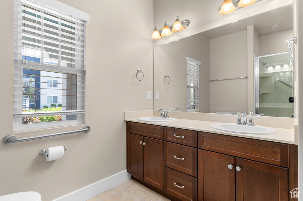 Bathroom featuring tile patterned floors, double vanity, baseboards, a shower with door, and toilet