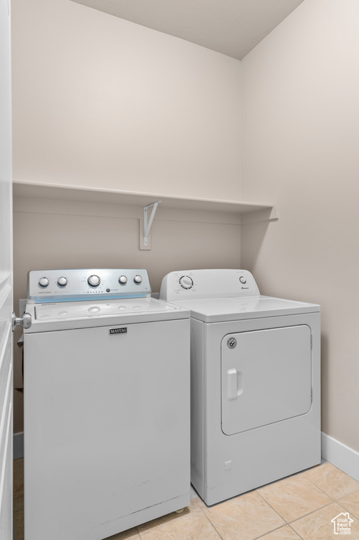 Laundry area featuring washing machine and dryer, light tile patterned floors, and baseboards