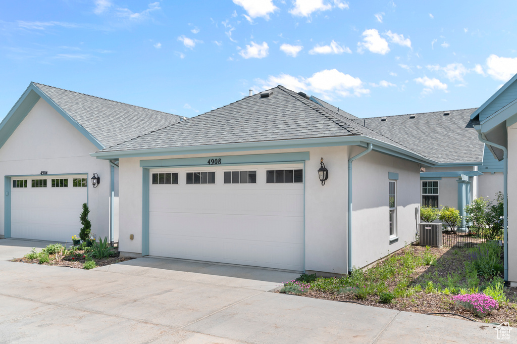 View of front of property with roof with shingles, a garage, central AC unit, concrete driveway, and stucco siding