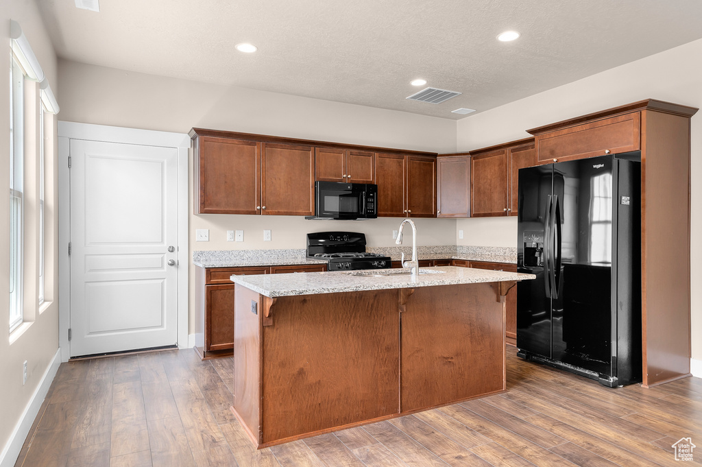 Kitchen with black appliances, a sink, recessed lighting, a kitchen island with sink, and wood finished floors