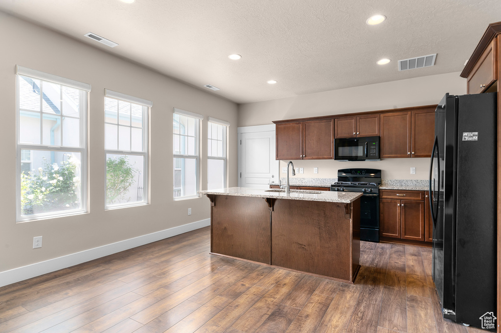 Kitchen featuring black appliances, a sink, baseboards, recessed lighting, and light stone counters