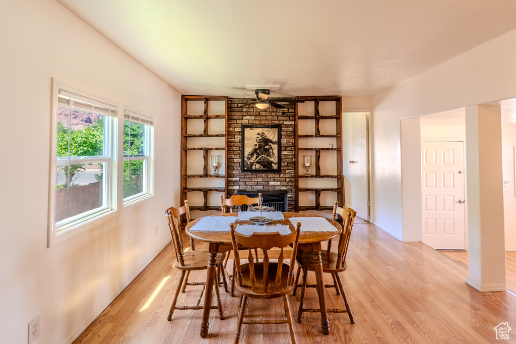 Dining space with light wood-style flooring, a brick fireplace, a ceiling fan, and built in features