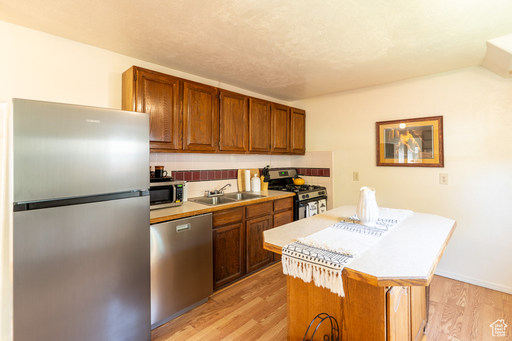 Kitchen featuring appliances with stainless steel finishes, a sink, decorative backsplash, a center island, and light wood finished floors