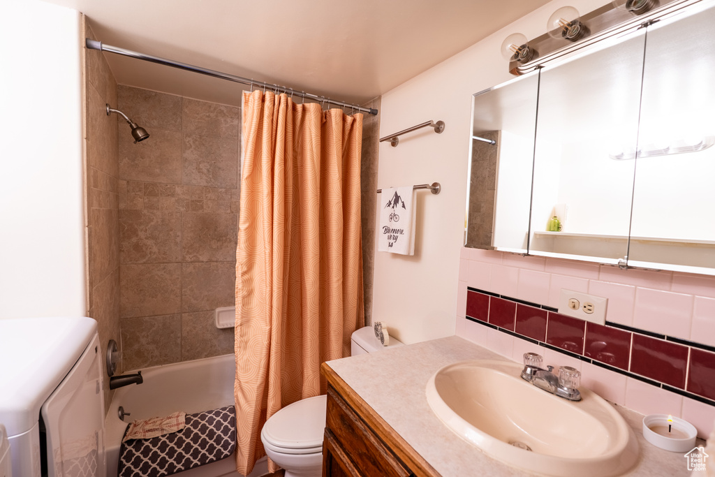 Full bathroom featuring toilet, shower / bath combination with curtain, vanity, washing machine and clothes dryer, and decorative backsplash
