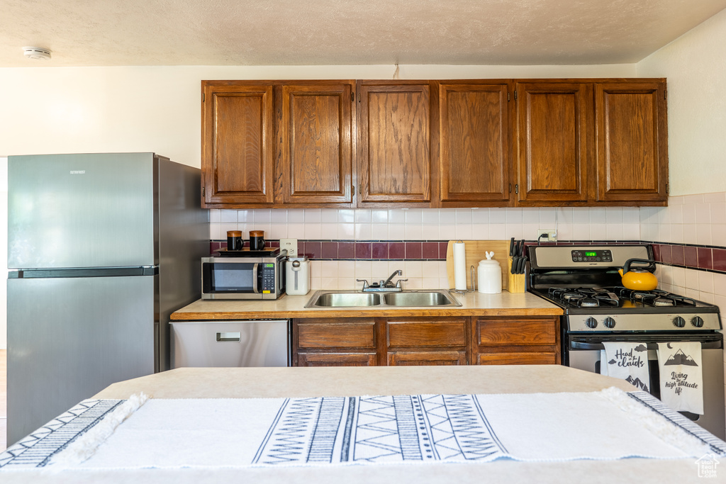Kitchen featuring stainless steel appliances, a sink, light countertops, and brown cabinetry