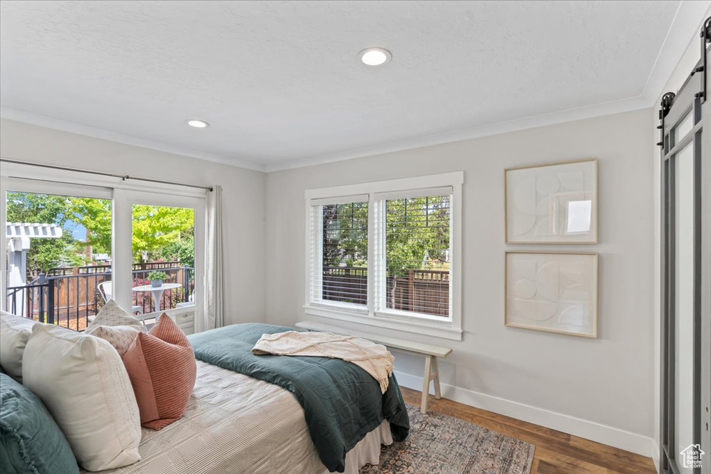 Bedroom with a barn door, baseboards, access to outside, crown molding, and wood finished floors