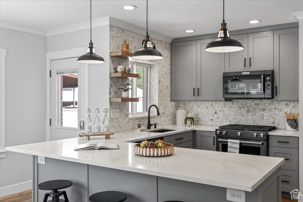 Kitchen featuring gray cabinetry, stainless steel appliances, open shelves, a sink, and a peninsula