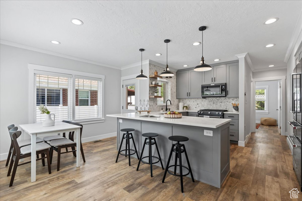 Kitchen featuring appliances with stainless steel finishes, gray cabinetry, a kitchen breakfast bar, light countertops, and wood finished floors