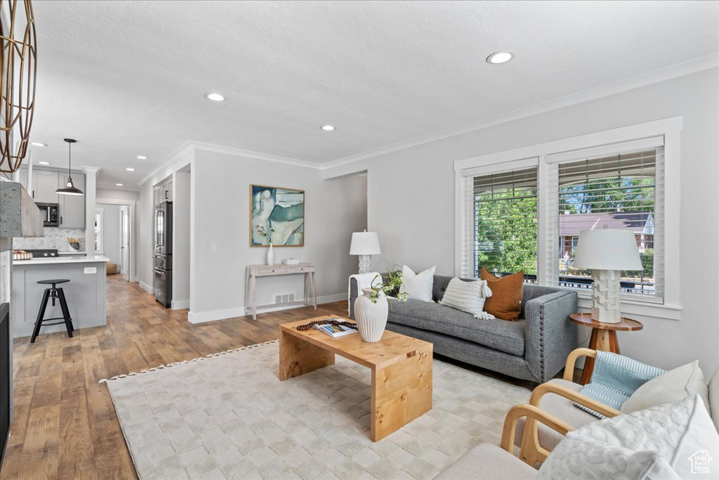 Living area featuring light wood finished floors, crown molding, baseboards, and recessed lighting