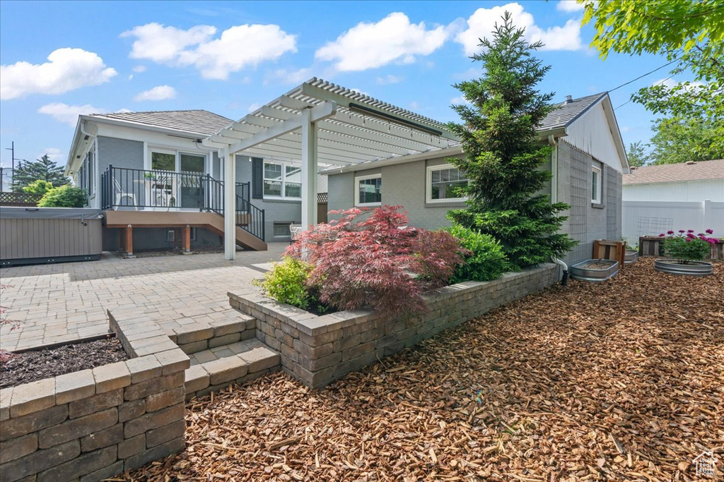 Rear view of property with a pergola, a patio area, and a hot tub