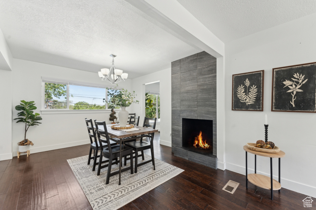 Dining space featuring a large fireplace, a textured ceiling, a chandelier, baseboards, and hardwood / wood-style floors