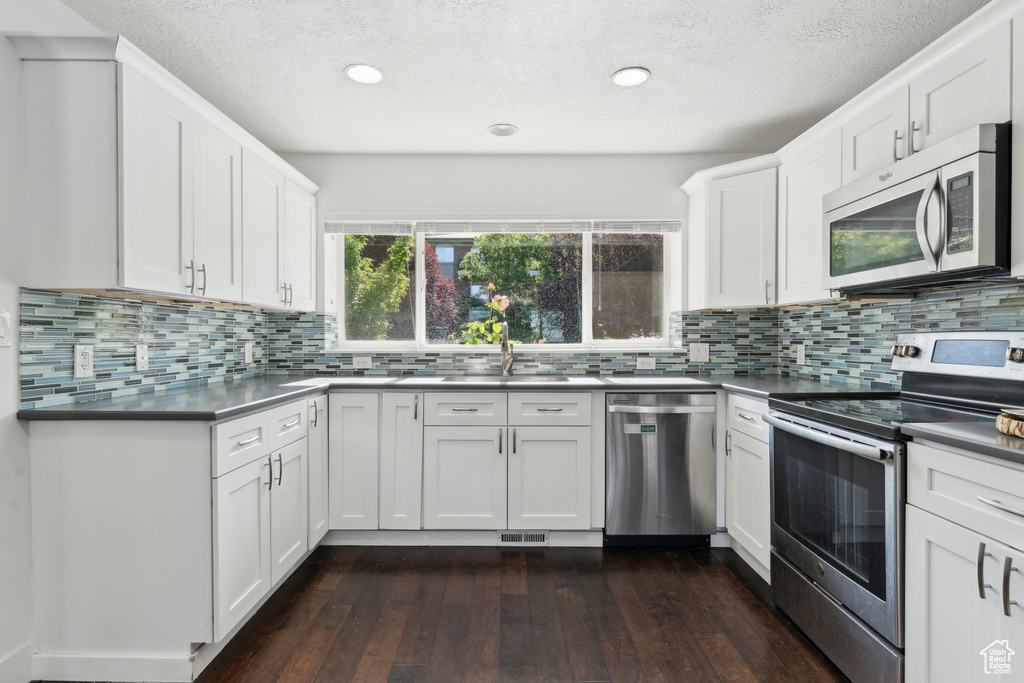Kitchen featuring stainless steel appliances, a sink, dark wood-type flooring, white cabinets, and a textured ceiling
