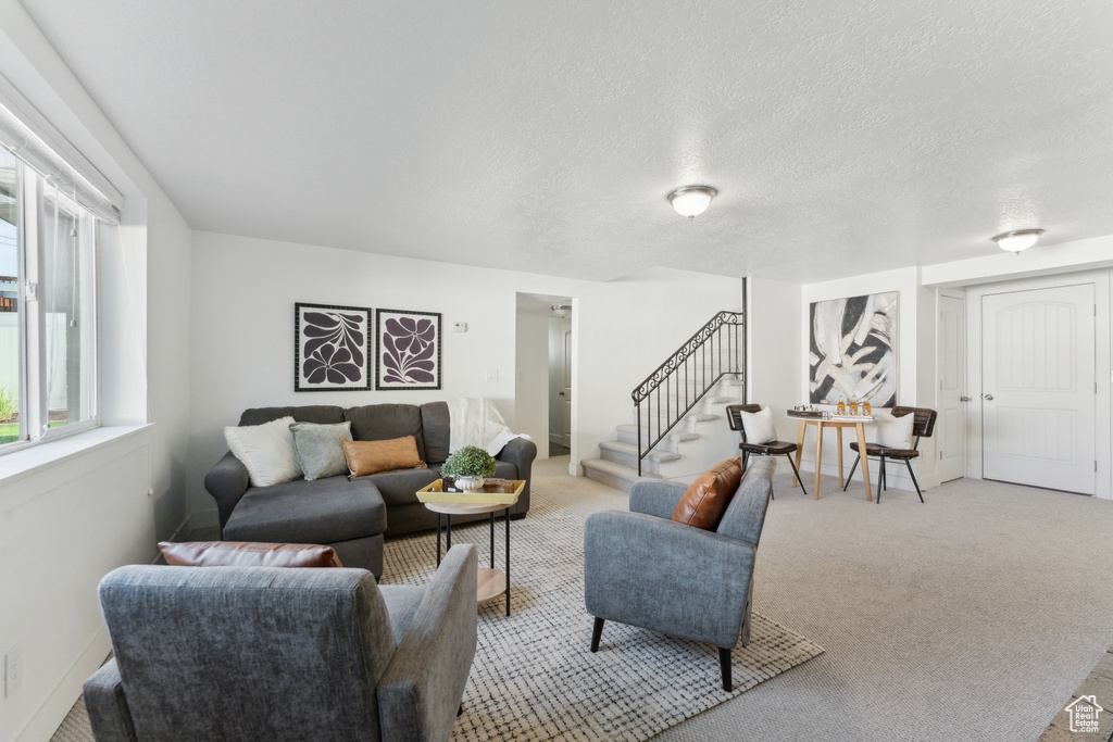 Living area with stairs, light colored carpet, a textured ceiling, and baseboards
