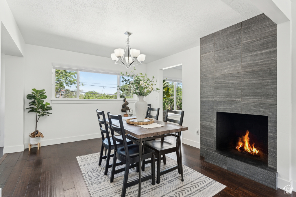 Dining space with a chandelier, hardwood / wood-style floors, baseboards, a fireplace, and a textured ceiling