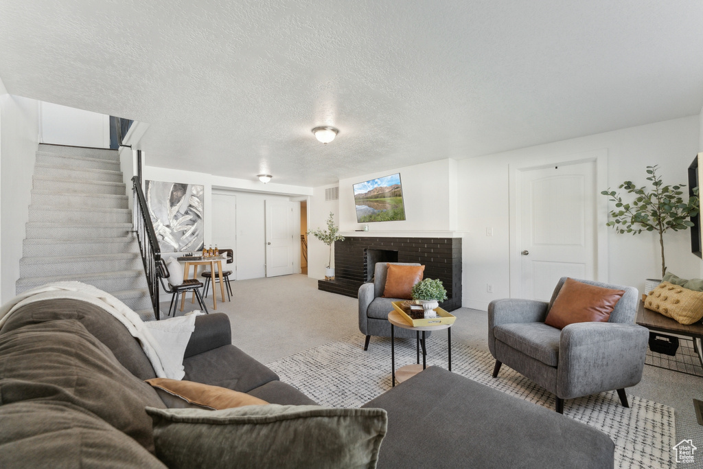 Living area with carpet, stairway, a fireplace, and a textured ceiling