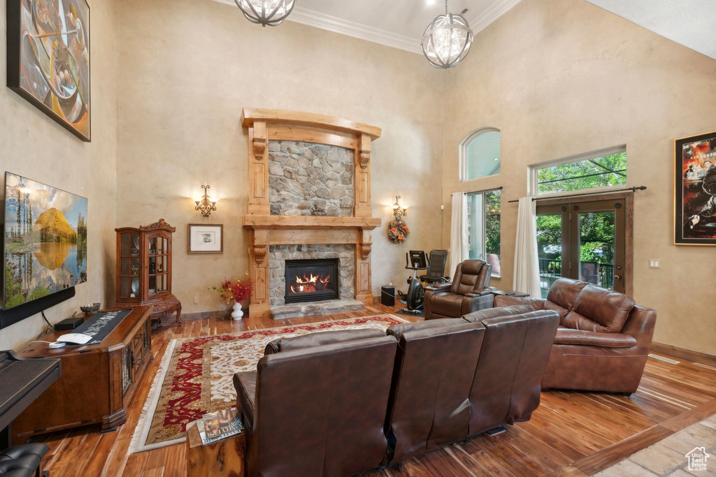Living area featuring a high ceiling, wood-type flooring, a stone fireplace, crown molding, and baseboards
