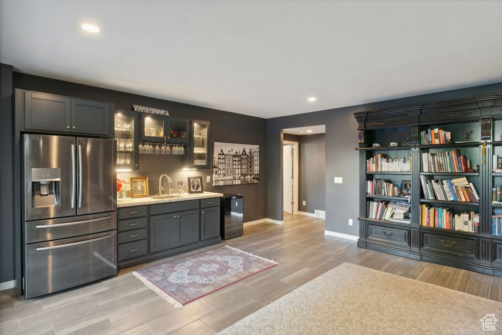 Indoor wet bar featuring stainless steel refrigerator with ice dispenser, baseboards, light wood finished floors, recessed lighting, and fridge