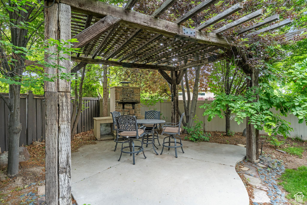 Fenced backyard with an outdoor stone fireplace, a patio, outdoor dining area, and a pergola