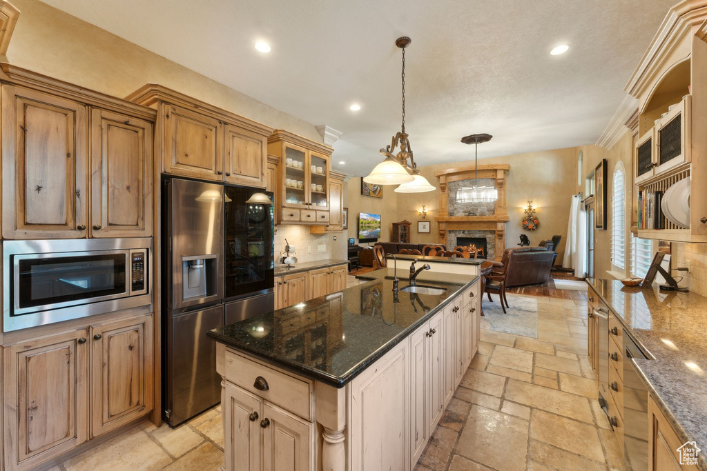 Kitchen with appliances with stainless steel finishes, stone tile flooring, a sink, recessed lighting, and a lit fireplace