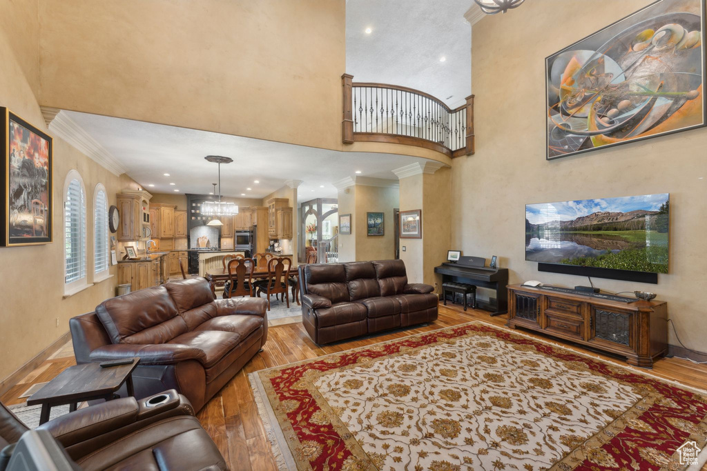 Living room with a high ceiling, light wood-style flooring, crown molding, plenty of natural light, and recessed lighting