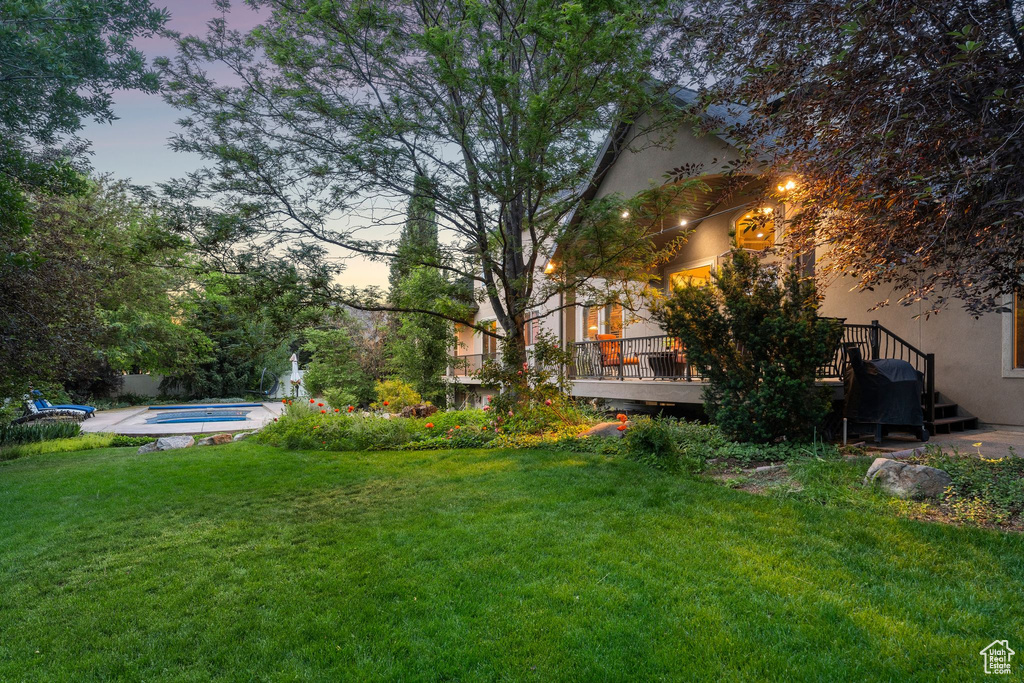 View of green lawn with a wooden deck, a hot tub, and an outdoor pool