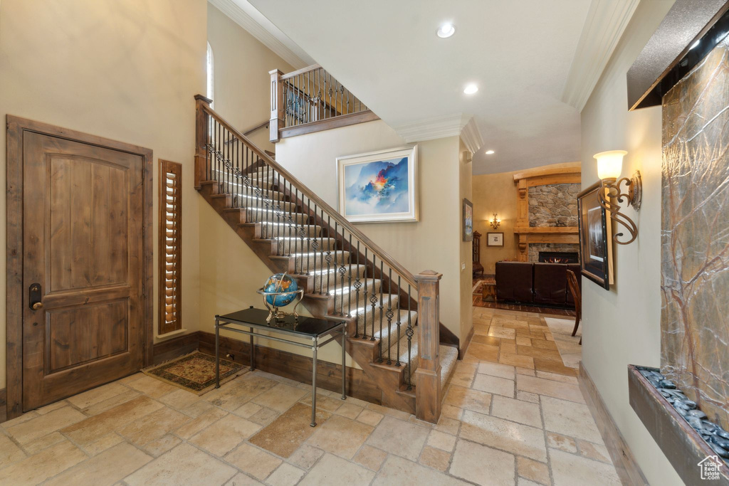 Stairs featuring stone tile floors, ornamental molding, recessed lighting, a stone fireplace, and baseboards