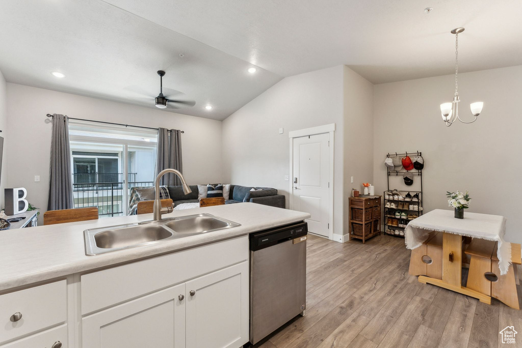 Kitchen featuring dishwasher, a sink, vaulted ceiling, light wood-style flooring, and white cabinetry