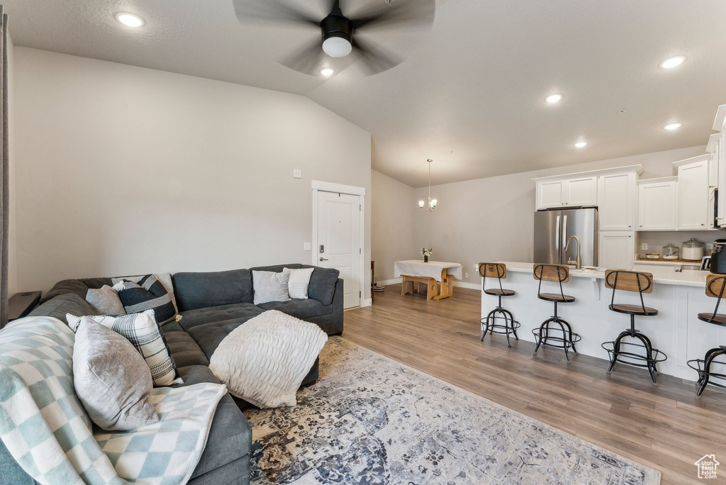 Living room with light wood finished floors, ceiling fan, vaulted ceiling, recessed lighting, and baseboards