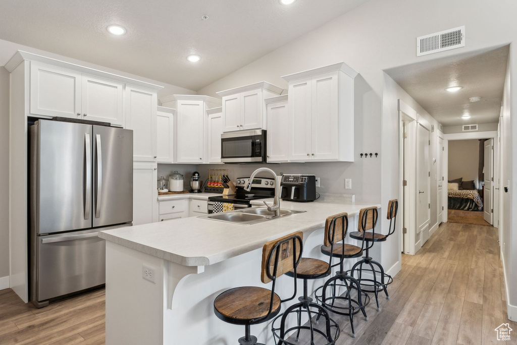 Kitchen featuring stainless steel appliances, a sink, light countertops, light wood finished floors, and white cabinetry