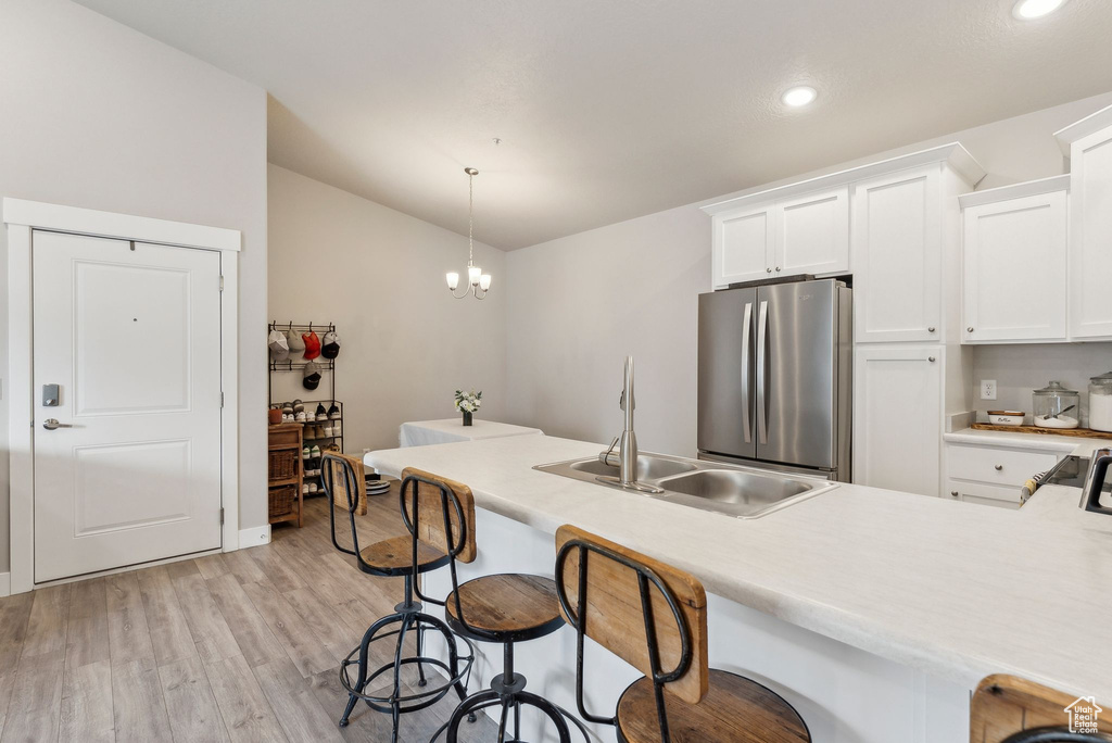 Kitchen featuring freestanding refrigerator, a sink, a breakfast bar, light wood-style floors, and light countertops