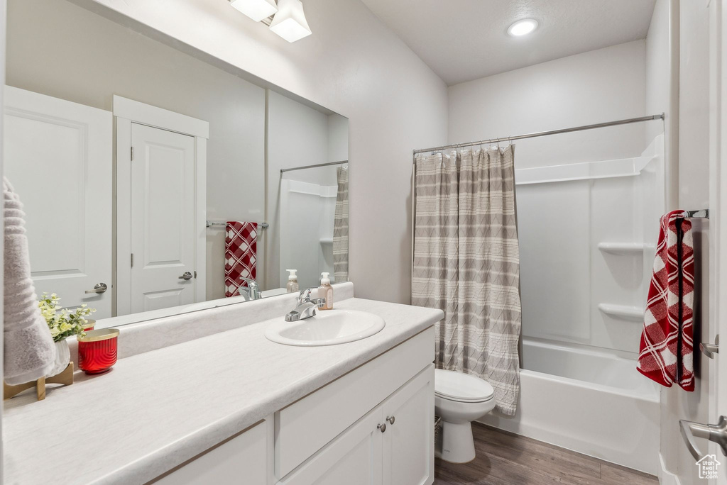 Bathroom with vanity, wood finished floors, shower / bath combination with curtain, toilet, and recessed lighting