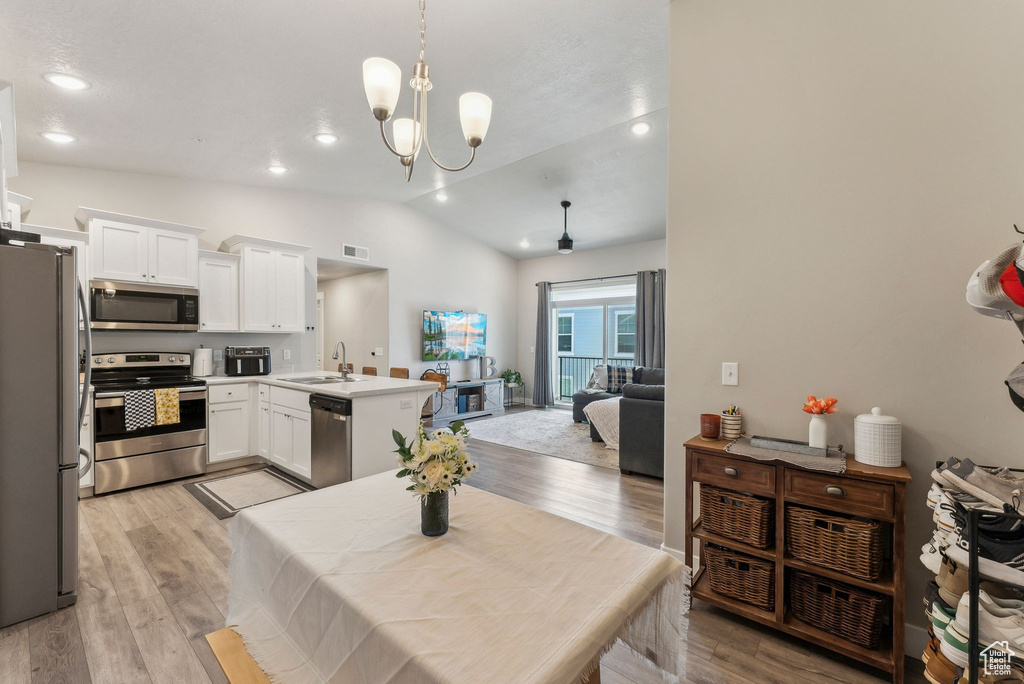 Kitchen with appliances with stainless steel finishes, a peninsula, open floor plan, white cabinetry, and vaulted ceiling