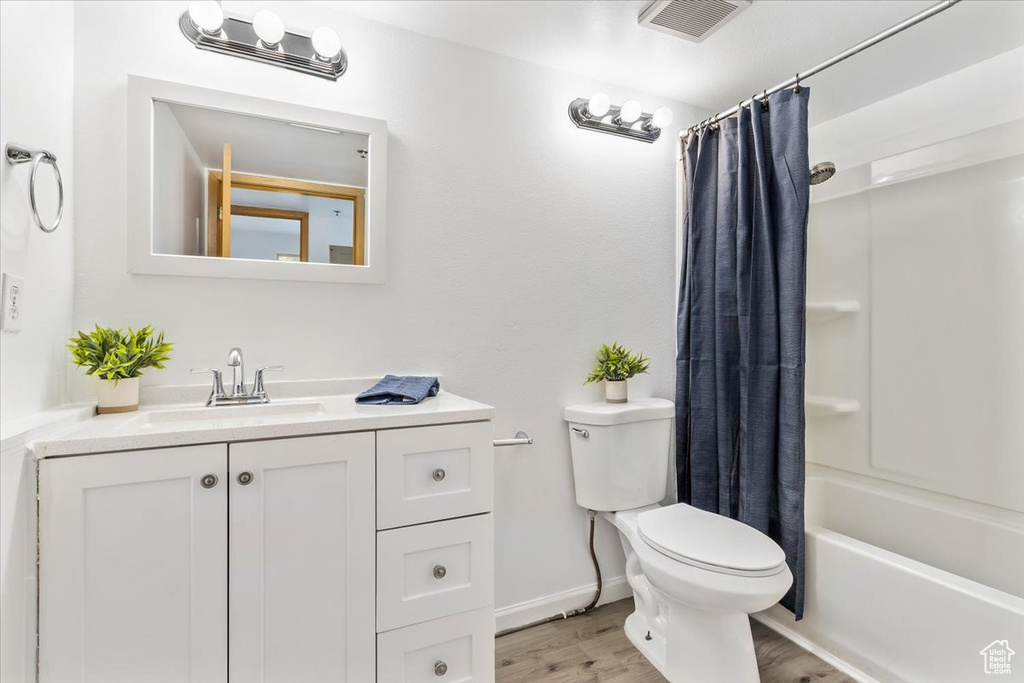 Bathroom with toilet, wood finished floors, vanity, and shower / bath combo with shower curtain