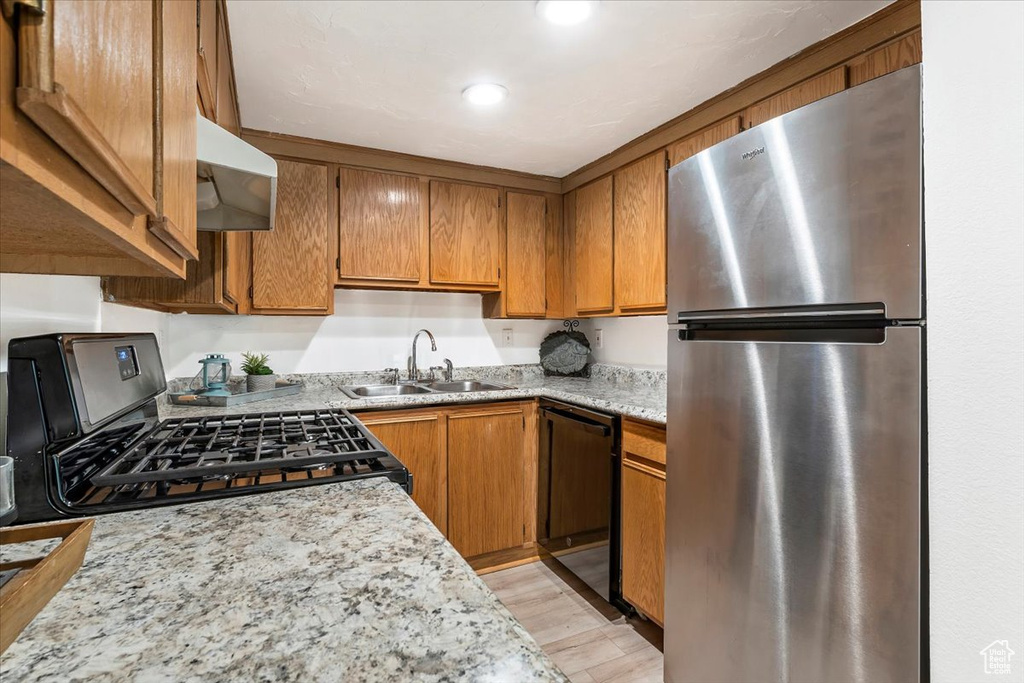 Kitchen featuring appliances with stainless steel finishes, range hood, a sink, brown cabinetry, and recessed lighting