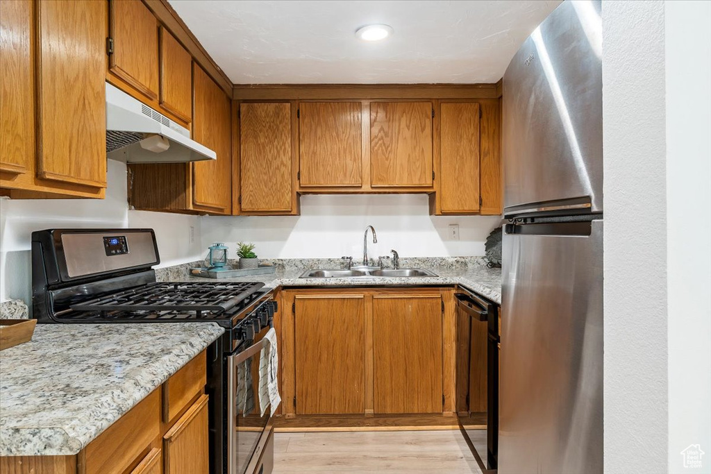 Kitchen featuring appliances with stainless steel finishes, a sink, under cabinet range hood, light wood-style flooring, and brown cabinets