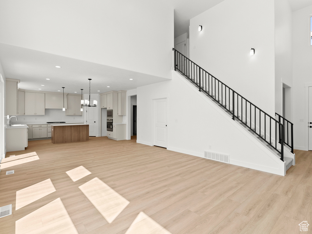 Unfurnished living room featuring light wood-type flooring, a high ceiling, stairway, recessed lighting, and a chandelier