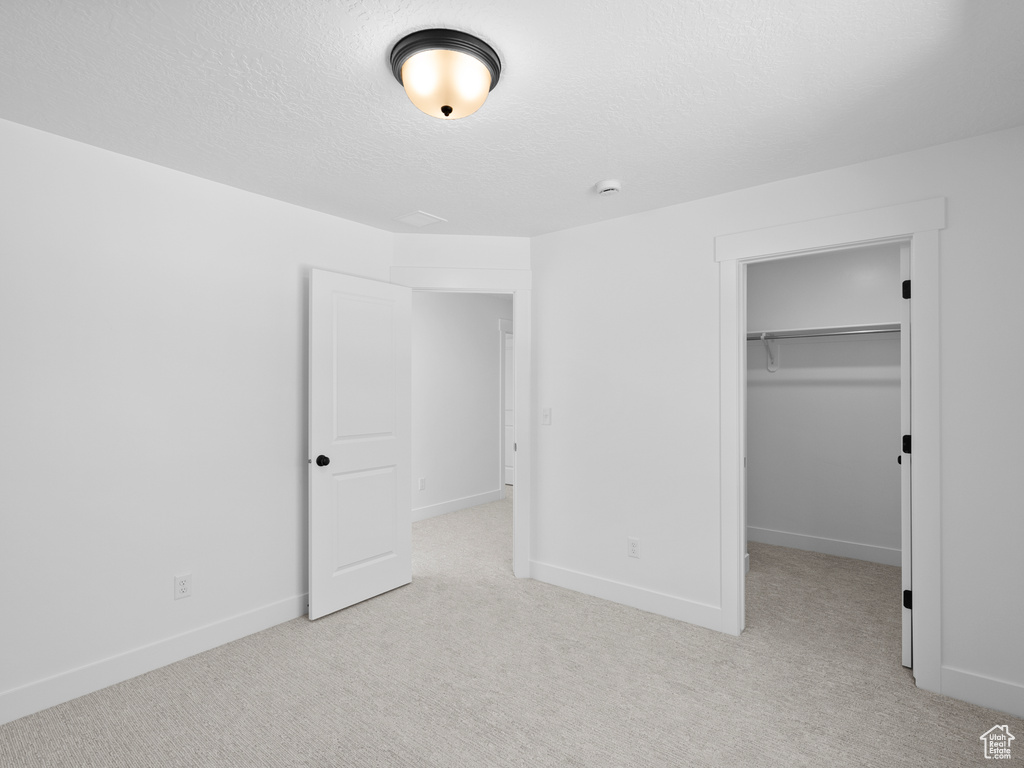 Unfurnished bedroom with carpet flooring, a spacious closet, a textured ceiling, and a closet