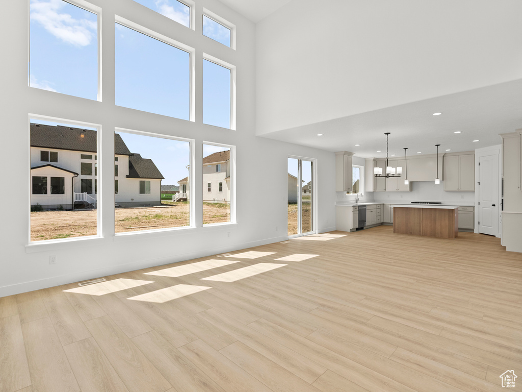 Unfurnished living room with light wood-type flooring, recessed lighting, and a towering ceiling