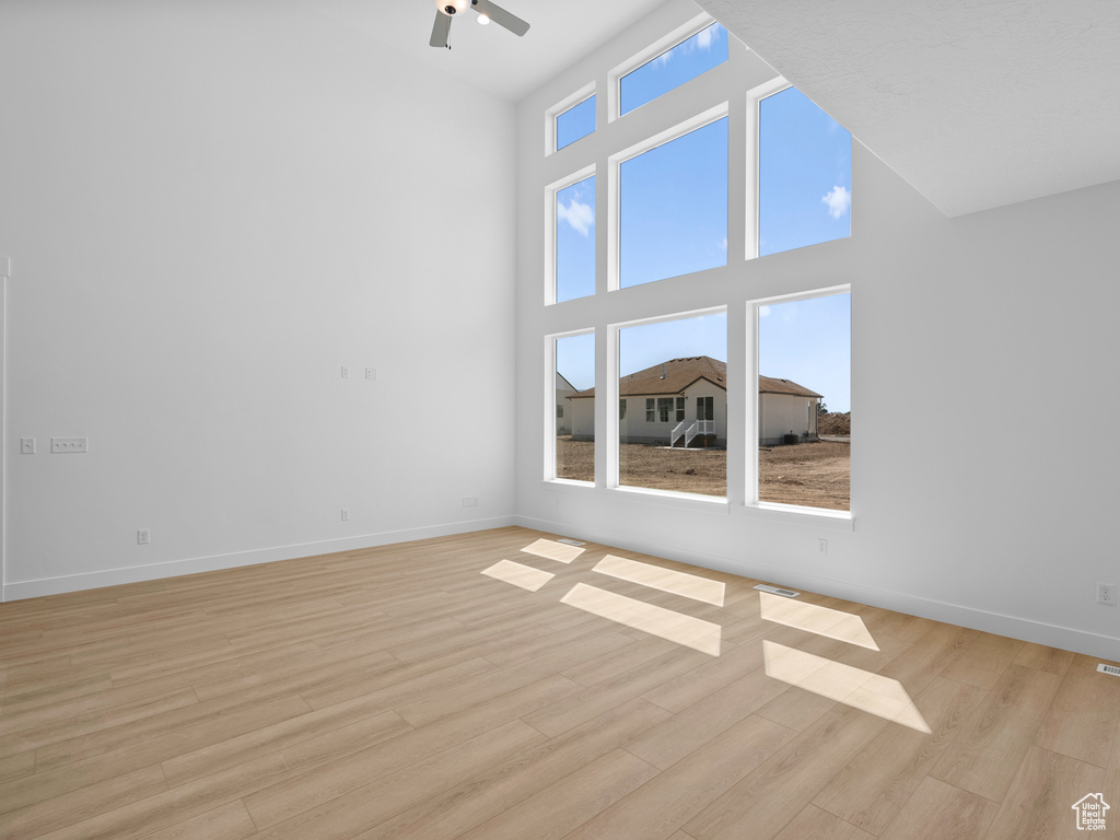Empty room featuring light wood-type flooring, a towering ceiling, and a ceiling fan