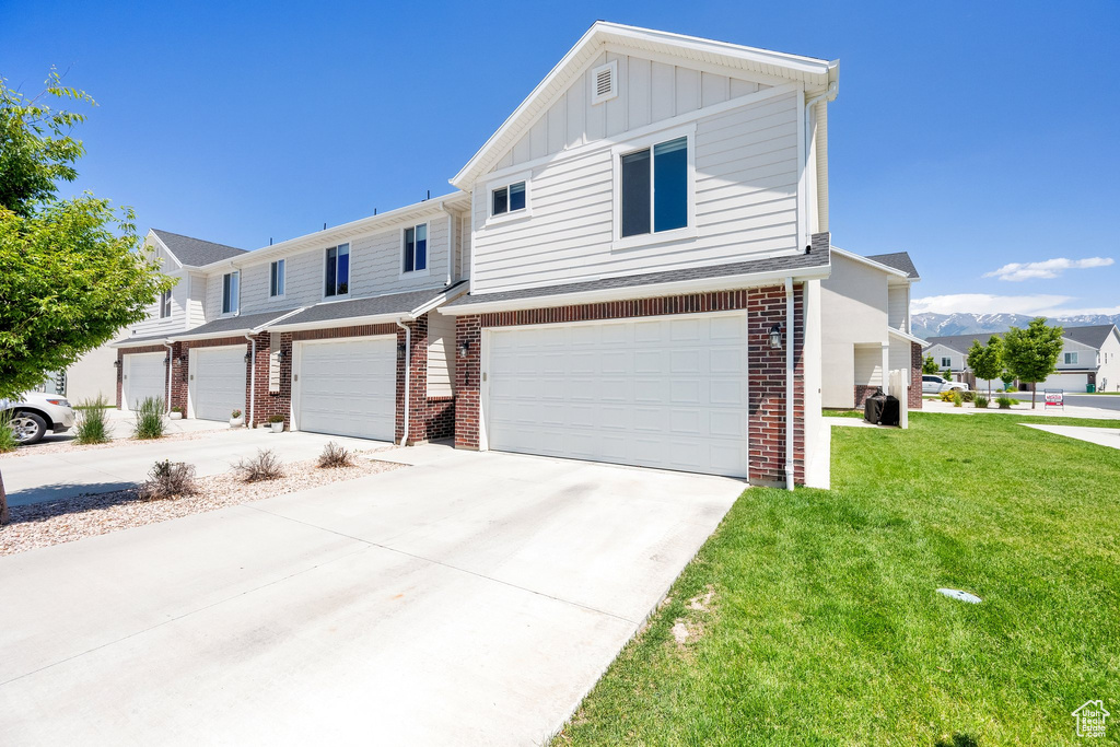View of front of home featuring brick siding, an attached garage, board and batten siding, and a front lawn