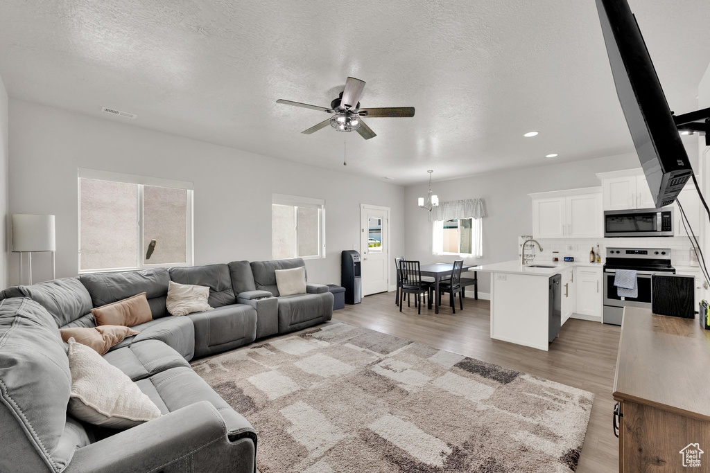 Living room with a ceiling fan, recessed lighting, light wood finished floors, and a textured ceiling