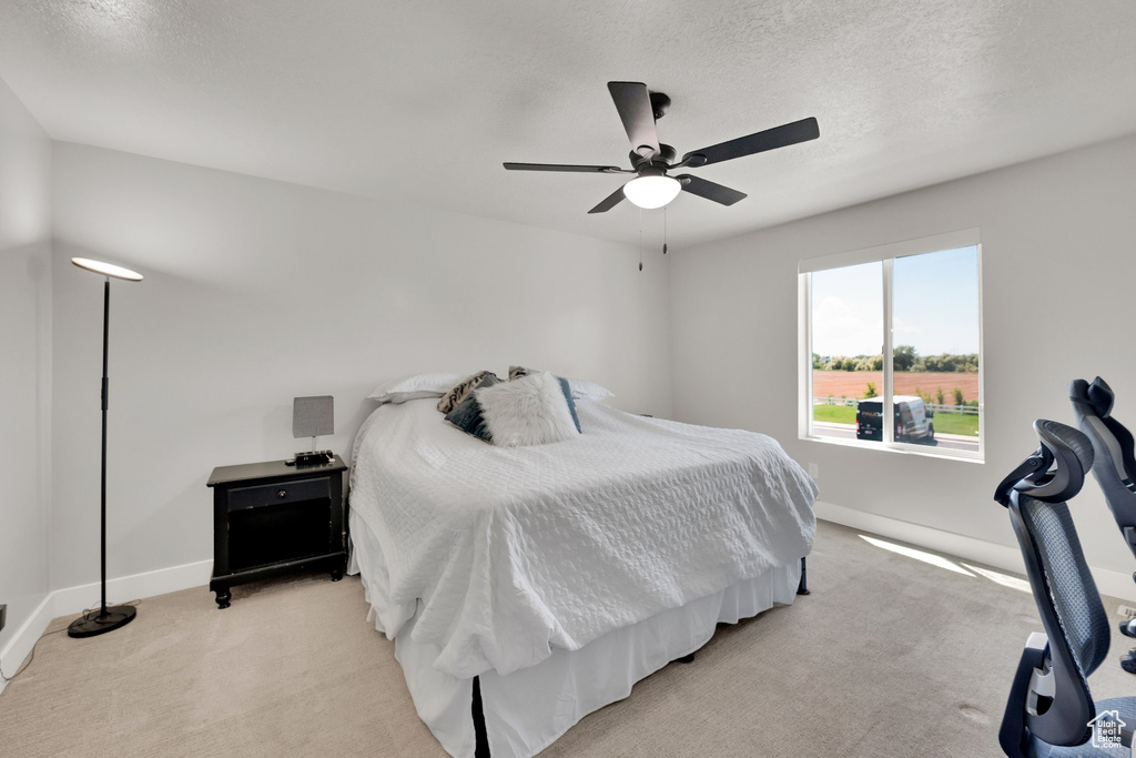 Bedroom featuring light colored carpet, baseboards, a ceiling fan, and a textured ceiling