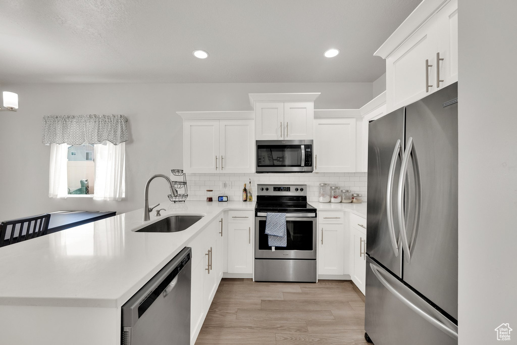 Kitchen with appliances with stainless steel finishes, a sink, a peninsula, light wood finished floors, and backsplash