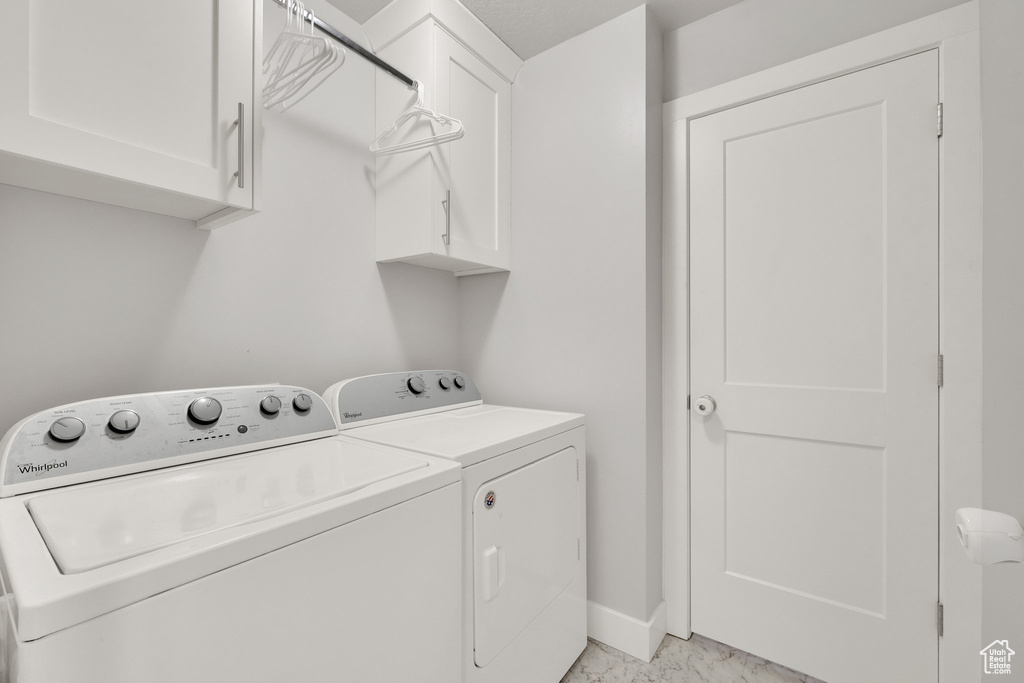 Laundry area with washing machine and dryer, cabinet space, light marble finish flooring, and baseboards