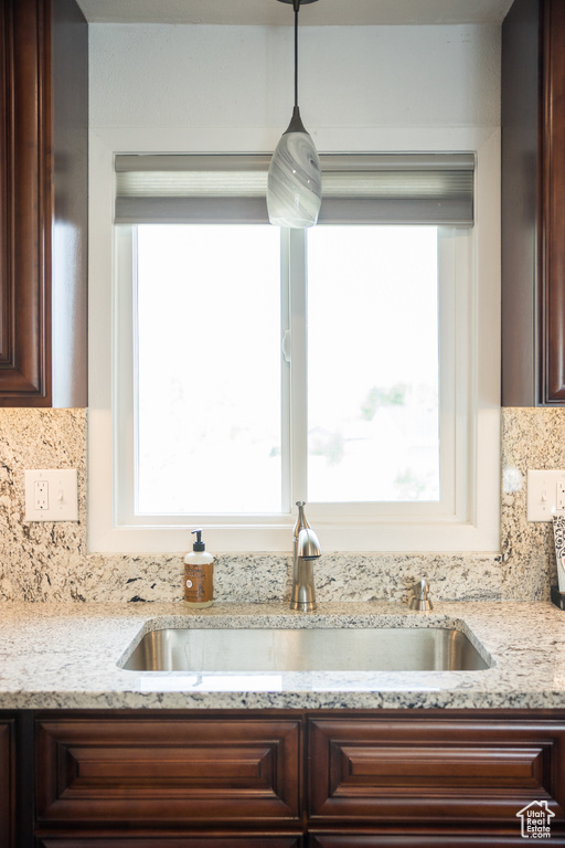 Kitchen with a sink, dark brown cabinets, tasteful backsplash, and light stone countertops