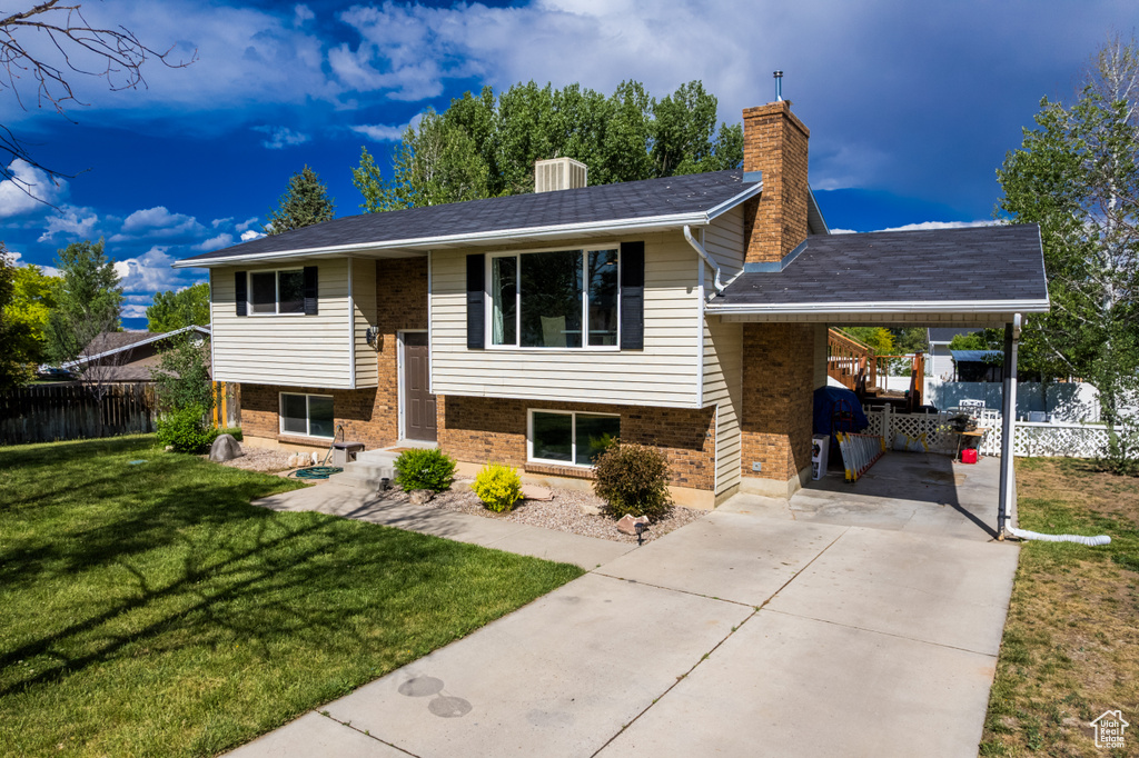 Raised ranch featuring concrete driveway, brick siding, a chimney, and a carport