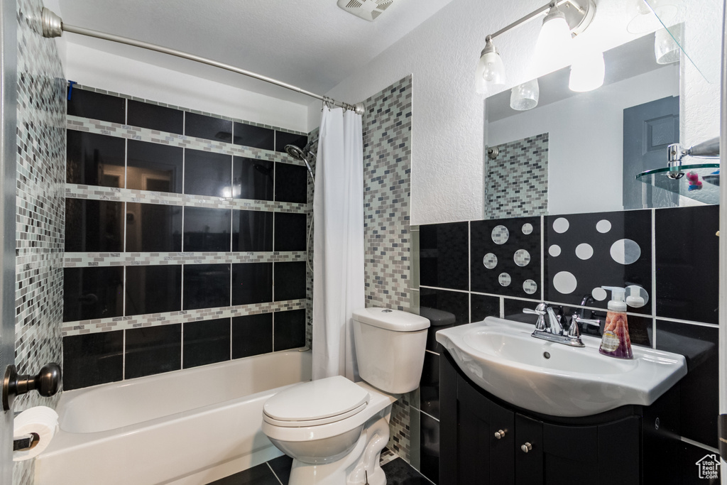 Bathroom featuring shower / bathtub combination with curtain, vanity, toilet, and a textured wall