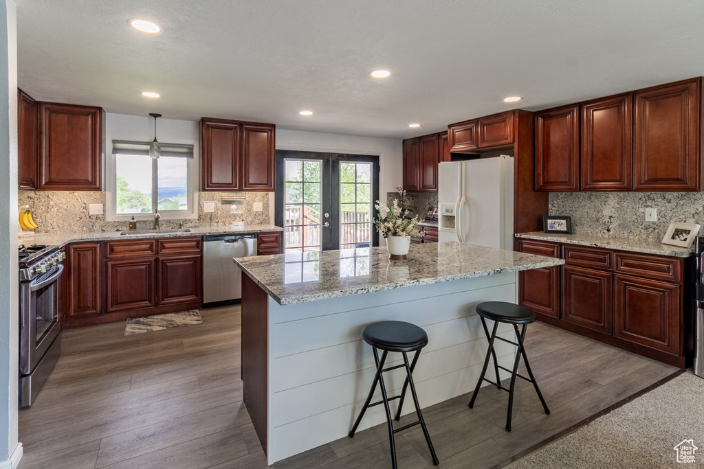 Kitchen featuring stainless steel appliances, wood finished floors, backsplash, a breakfast bar area, and light stone countertops