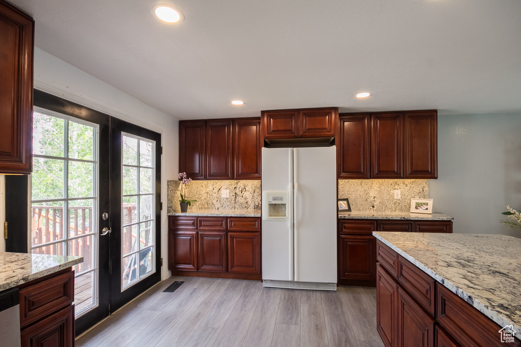 Kitchen with white refrigerator with ice dispenser, french doors, tasteful backsplash, light wood finished floors, and light stone countertops